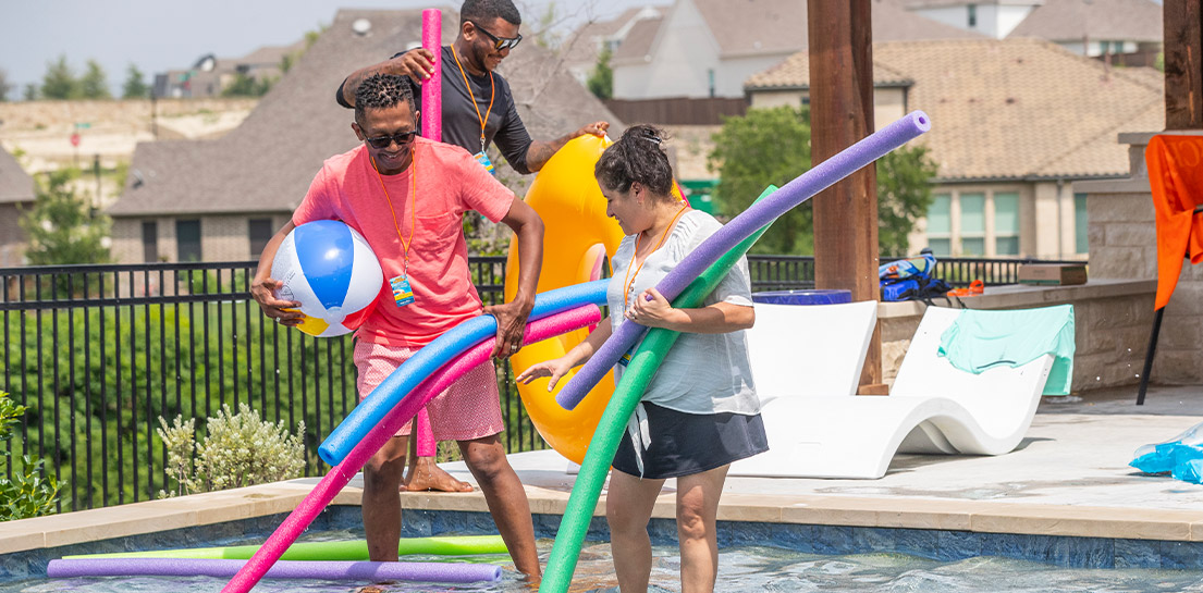 Three adults removing kids toys from pool after swimming is done